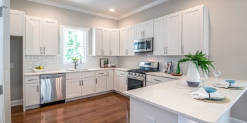 clean white kitchen with wooden floor|spacious kitchen in white tones and large window|Y29jaW5hIGVuIGJsYW5jbyB5IG1hZGVyYSBjb24gdGFidXJldGVzIGFsdG9zIG1ldMOhbGljb3M=|countertop with table and salads|white kitchen with white tile and wood counter top