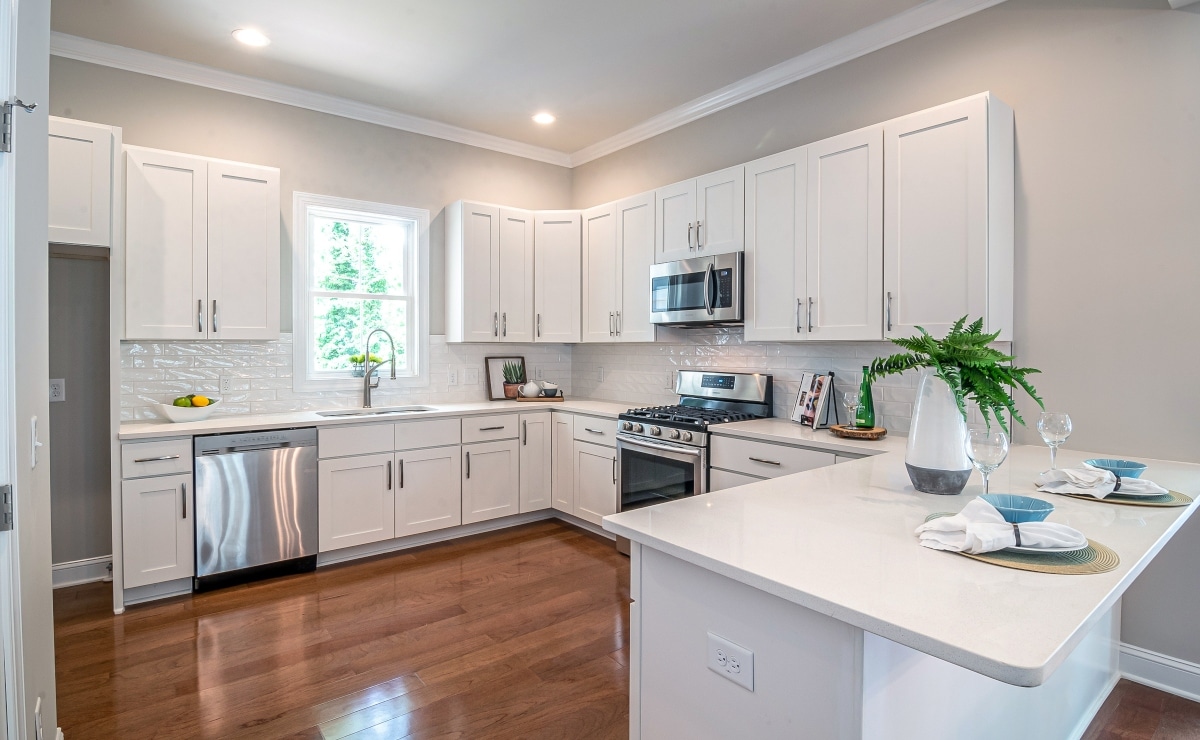 clean white kitchen with wooden floor|spacious kitchen in white tones and large window|Y29jaW5hIGVuIGJsYW5jbyB5IG1hZGVyYSBjb24gdGFidXJldGVzIGFsdG9zIG1ldMOhbGljb3M=|countertop with table and salads|white kitchen with white tile and wood counter top