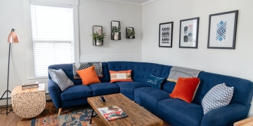 sofa in blue tones with orange cushions in a living room with carpet in the same tones