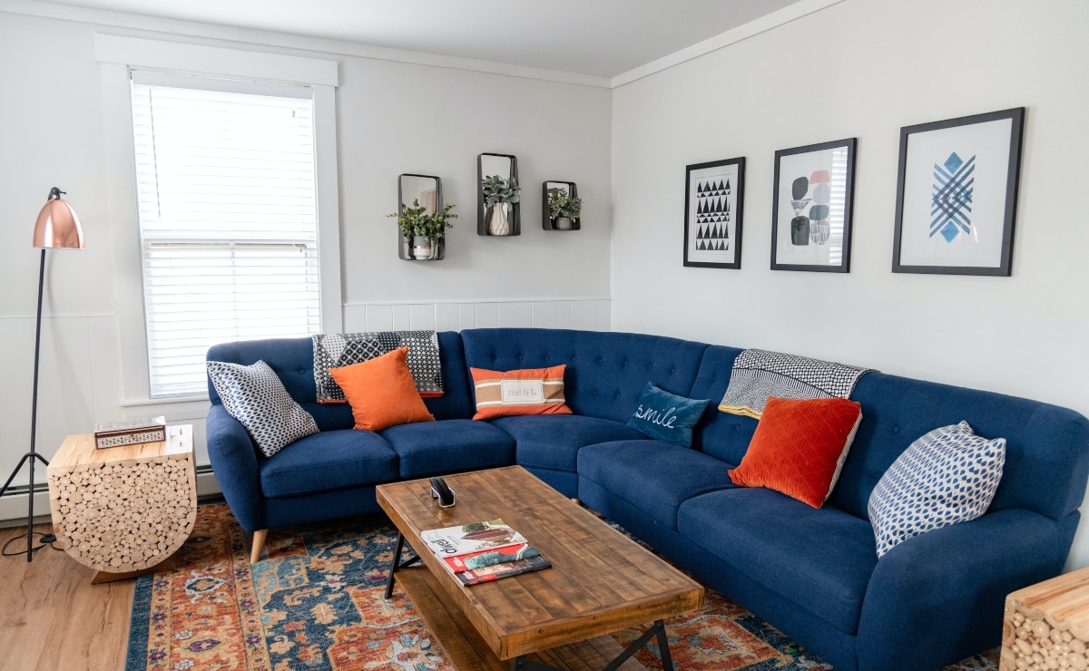 sofa in blue tones with orange cushions in a living room with carpet in the same tones