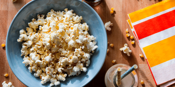 Bowl de palomitas junto a un vaso con sorbetes y una servilletas de colores.
