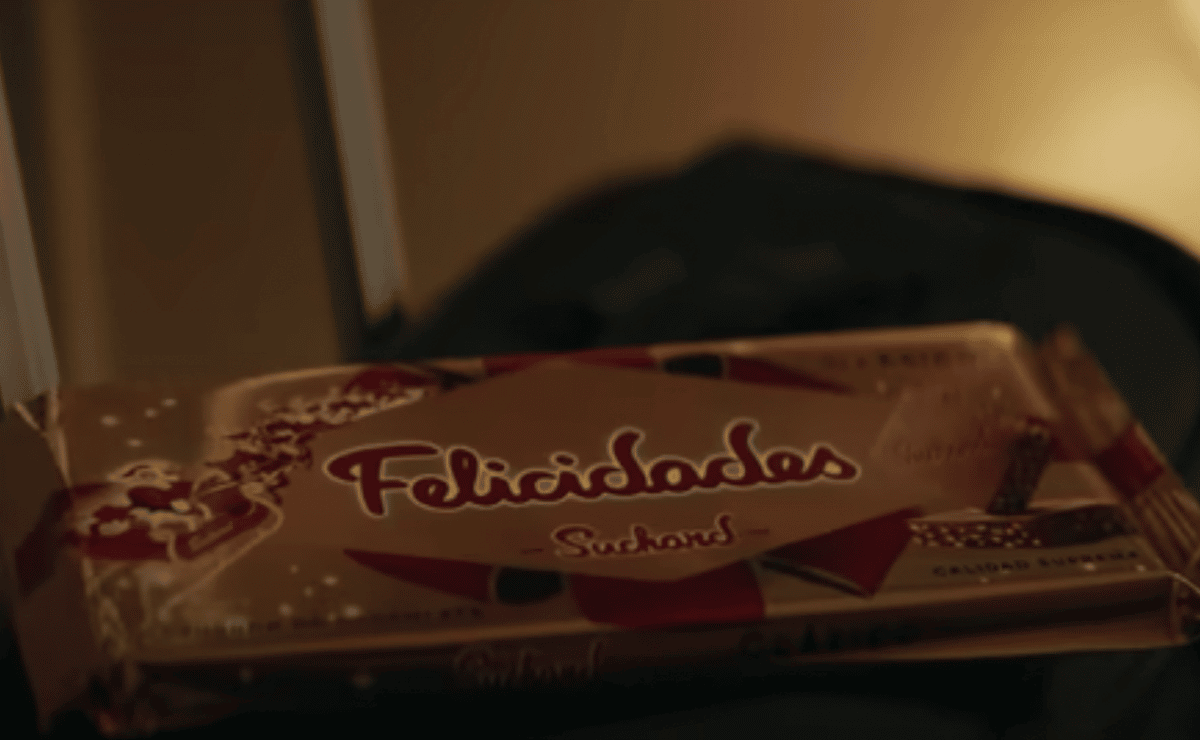 Tableta de turrón de chocolate Suchard encima de una maleta de viaje y con el mensaje de felicidades en su packaging.