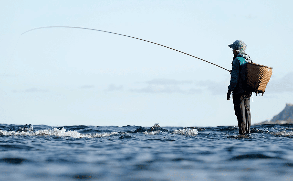 Hombre con un cesto a la espalda pescando a la orilla del mar.