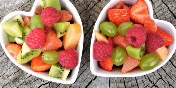 Dos bowls blancos con forma de corazón llenos de trocitos de frutas variadas.