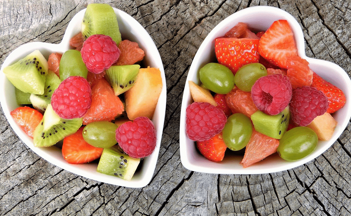Dos bowls blancos con forma de corazón llenos de trocitos de frutas variadas.