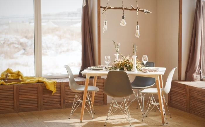 comedor pequeño con mesas y sillas escandinavas, bombillas colgando y gran ventana, en madera