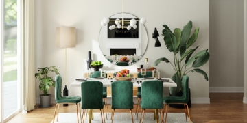 white rectangular dining table, with green chairs with wooden legs, in a room with mirror, lamp, carpet and plant.