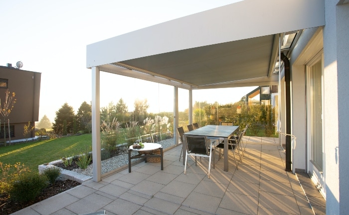 porche de casa gris, cubierto, con jardín y una gran mesa