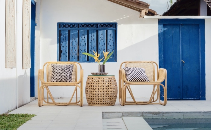 casa de verano blanca con detalles en azul, mesa y dos sillones con cojines y planta