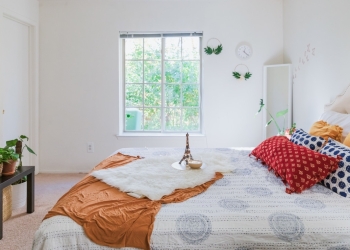 dormitorio con ventana, colcha blanca y manta y cojines coloridos