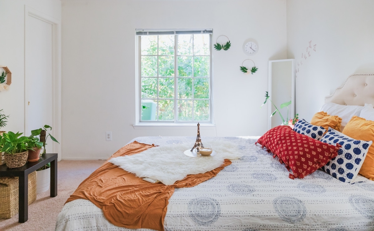 dormitorio con ventana, colcha blanca y manta y cojines coloridos