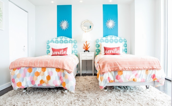 dormitorio de dos camas, colchas de circulos de colores, pared blanco con dos franjas azules y varios accesorios