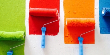 parde blanco con cuatro brochas que han pintado una franja verde, roja, naranja y azul