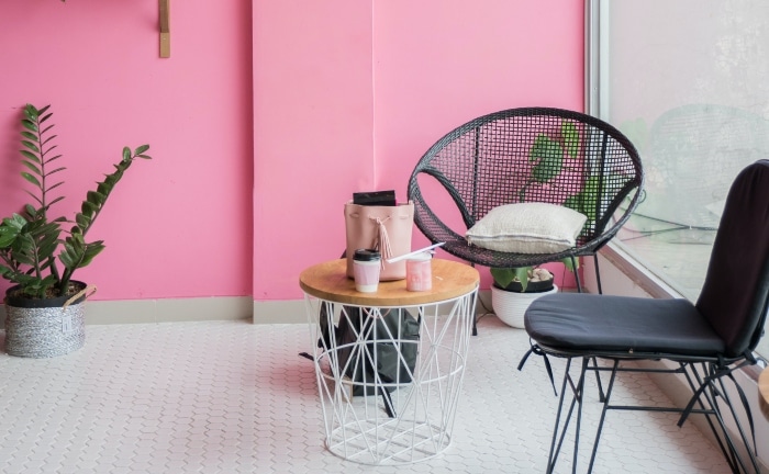 mesa y sillas de mimbre en negro, con planta en el suelo y pared rosa