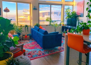 salón con sofá azul, cojines y sillas de colores, alfombra colorida y muchas plantas