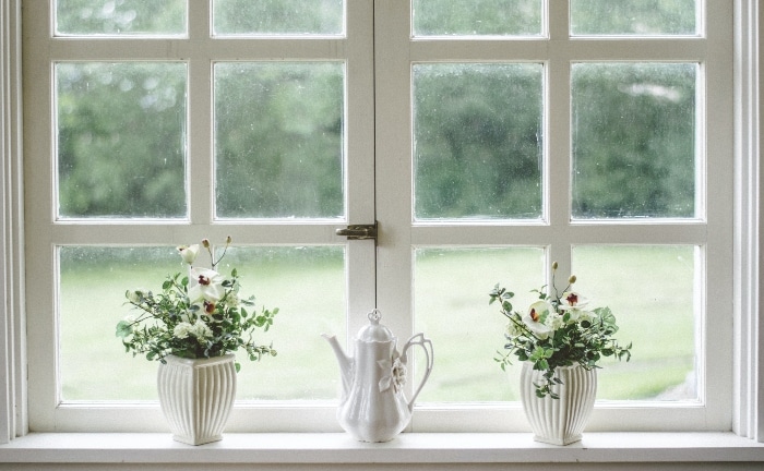 ventana blanca con jarrones de cerámica con flores y una tetera también de cerámica blanca