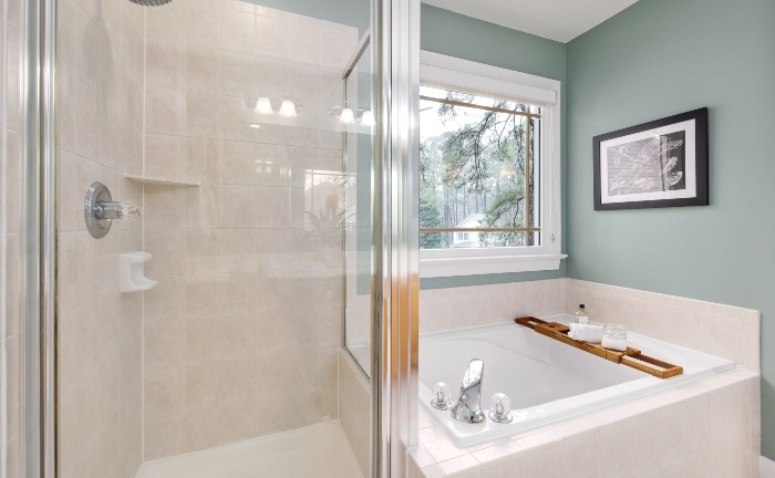 baño con pared verde, con ducha y amplia bañera cuadrada con una bandeja de madera con objetos decorativos