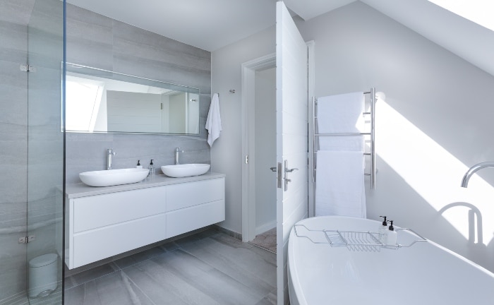 baño con bañera, lavabo doble en blancos, espejo y pared gris