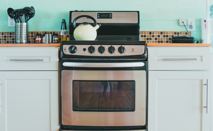 detalle de cocina con pared turquesa y gresite de colores ocres, con horno en primer plano y tetera beige en los fogones