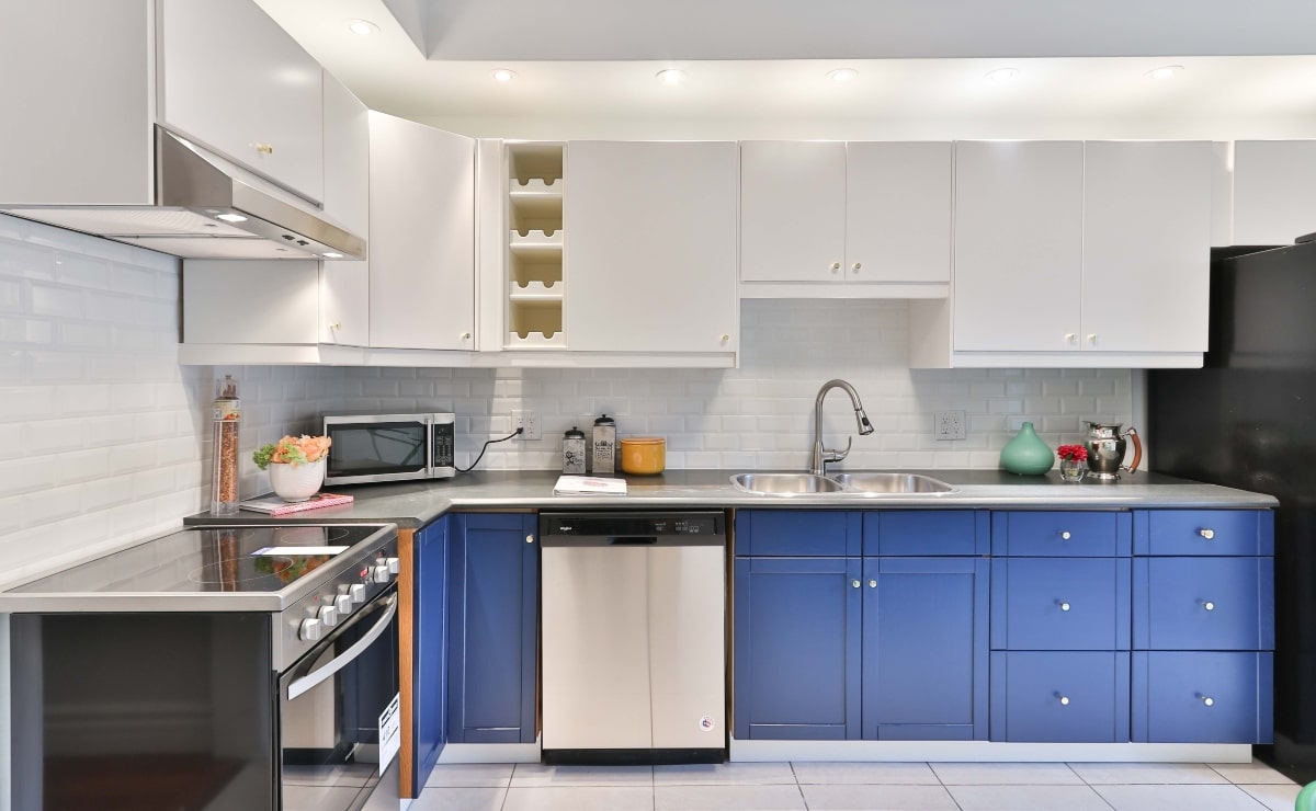 cocina moderna con electrodomésticos plateados, muebles superiores blancos e inferiores azules