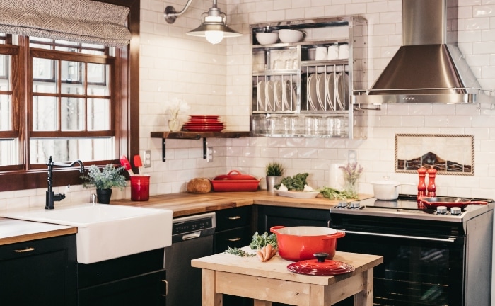 Kitchen in black and wood tones, with a hood and silver appliances, bench plates and some vegetables