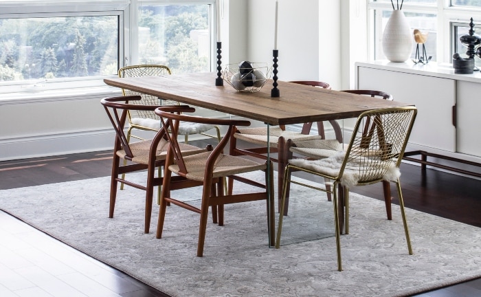 mesa de comedor con varias sillas, alginas de ellas modelo wishbone, alfombra neutra y mueble auxiliar con varios accesorios