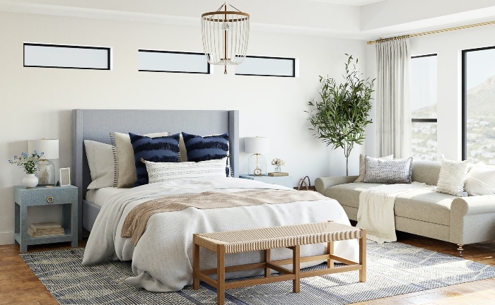 dormitorio en blancos y azules, con sofá blanci, planta y banco de madera a los pies de la cama