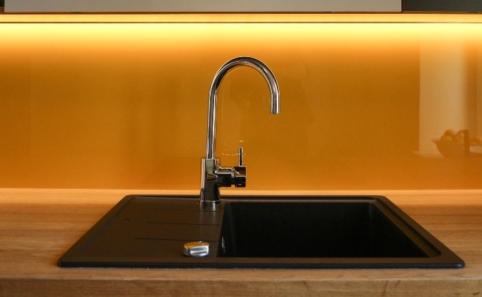 silver faucet detail with black sink and bright yellow wall