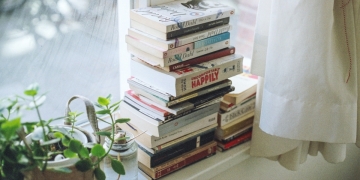 varios libros apilados en repisa de ventana blanca con una planta