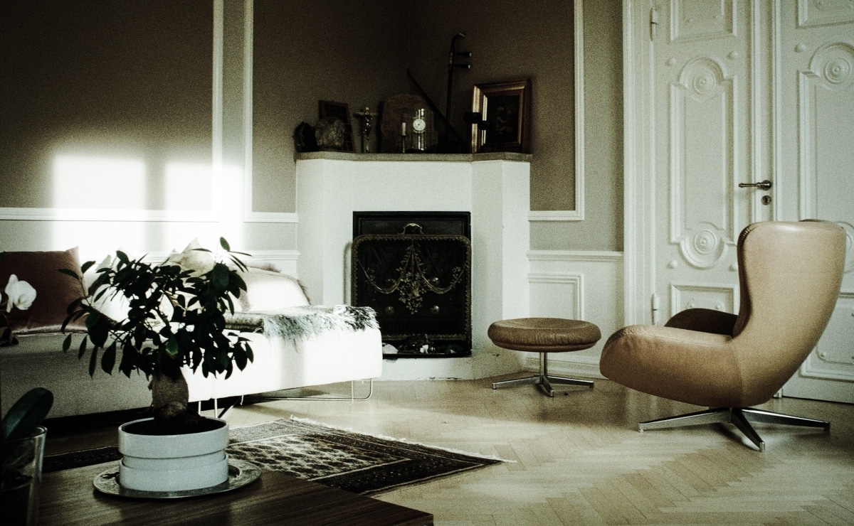 salón con chimenea en tonos beige, cuenta con mesa con planta y mesa auxiiar junto a la butaca